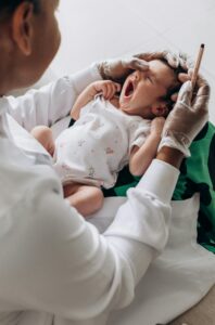 A newborn baby yawns during a health checkup by a doctor in a clinical setting.
