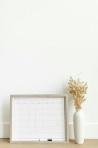 A minimalist setup featuring a framed calendar and decorative vase against a white background.
